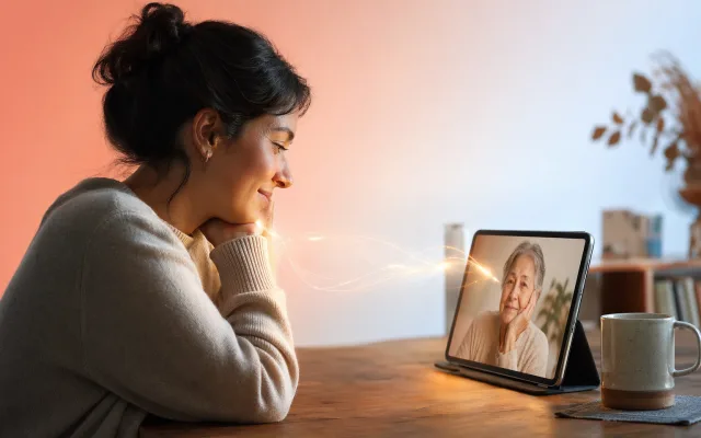 Adult child looking at a phone screen showing a video call with an older parent in a warmly lit room